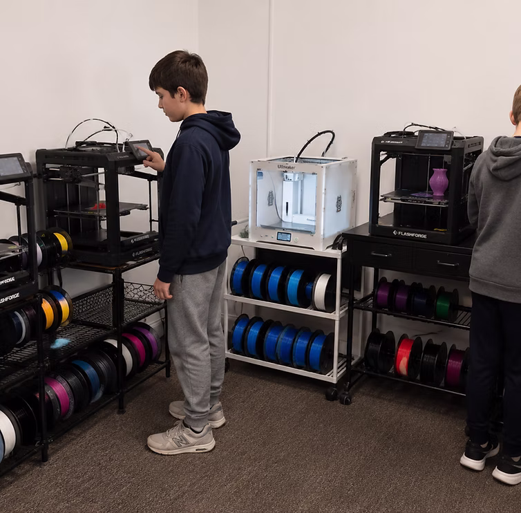 A student interacting with a 3D printer surrounded by racks of filament.